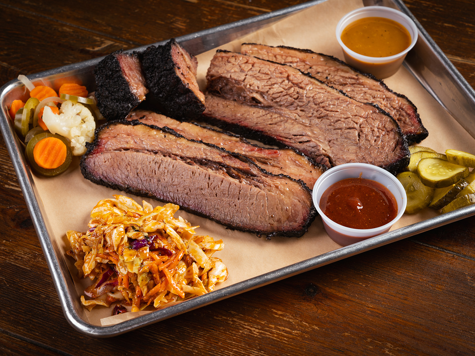 Beef brisket on a tray with pickles and sauce