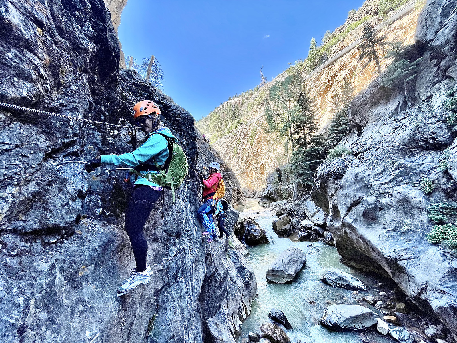 Two people climb a via ferrata over a stream