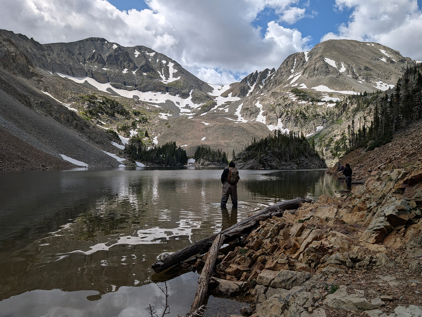A man stands at the edge of an alpine lake