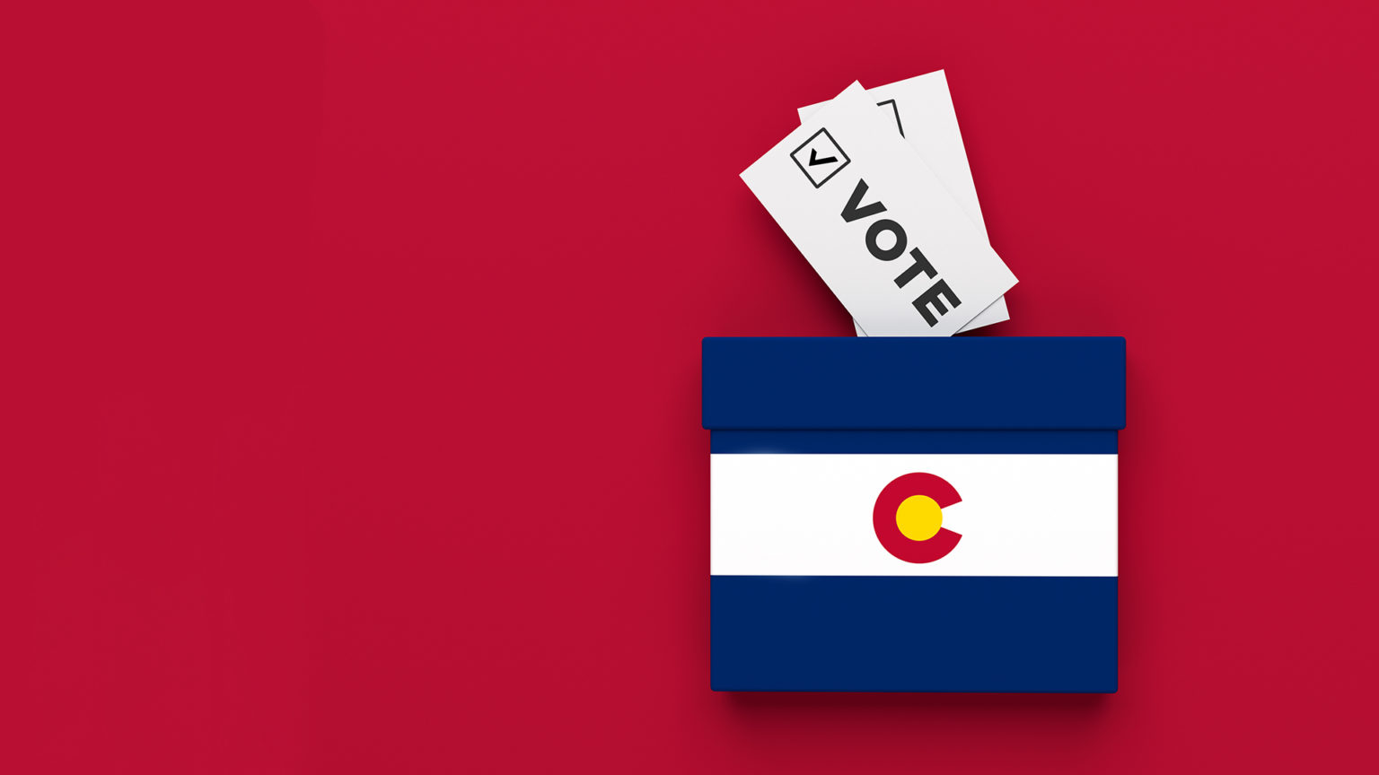 A Colorado flag emblazoned on an illustrated box sits on a red background. Two rudimentary "Vote" ballots are sticking out of it.