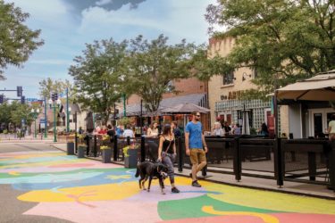 Two people and a dog walk through Olde Town Arvada