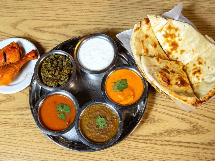 A plate of chicken, small metal bowls with various curries, and naan at best Indian restaurant.