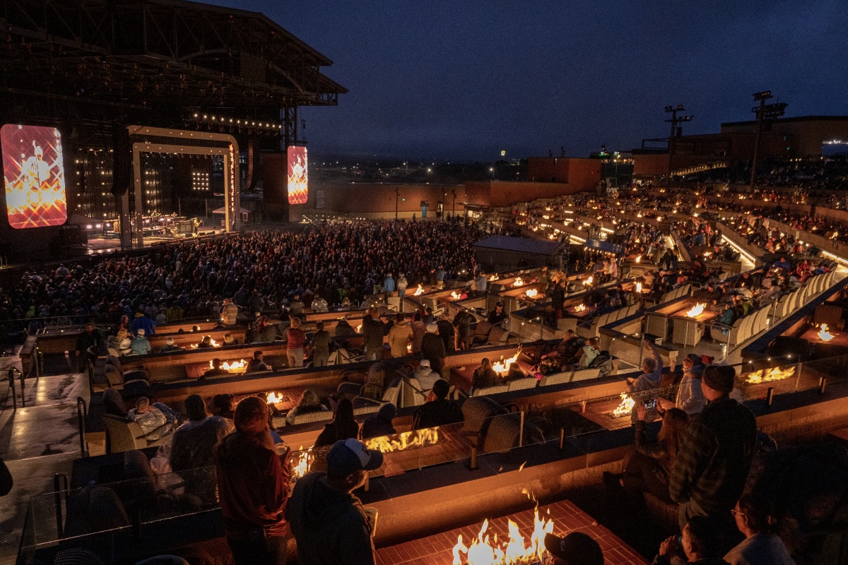 Concertgoers around fire pits face the stage