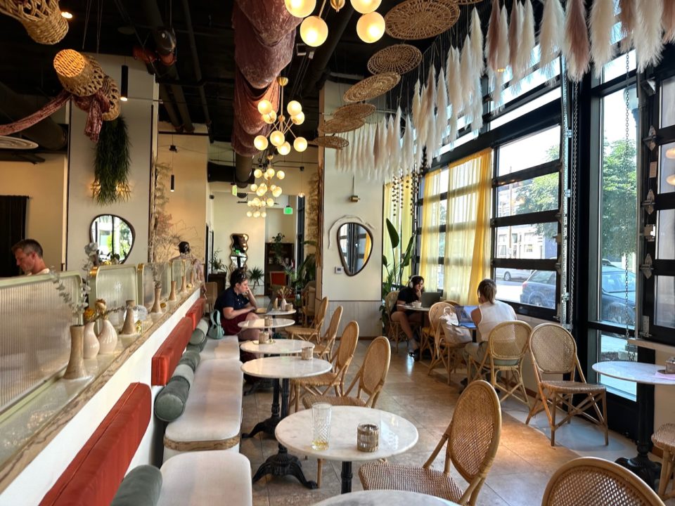 People work inside Flora, a bohemian-inspired coffee shop with large windows and wicker chairs