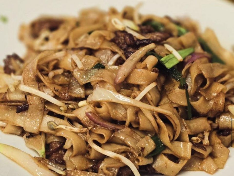 Closeup of a plate of Chinese sauced broad noodles with beef, bean sprouts, and other vegetables.