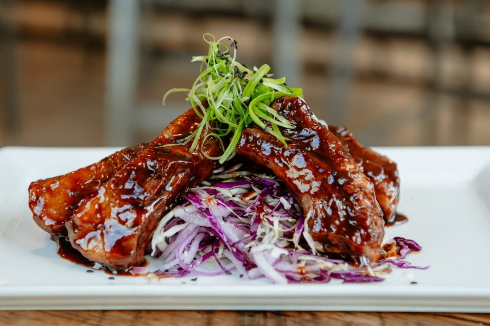 A plate of glazed pork ribs arranged tips up on a mound of shredded vegetables and topped with sliced green onion.