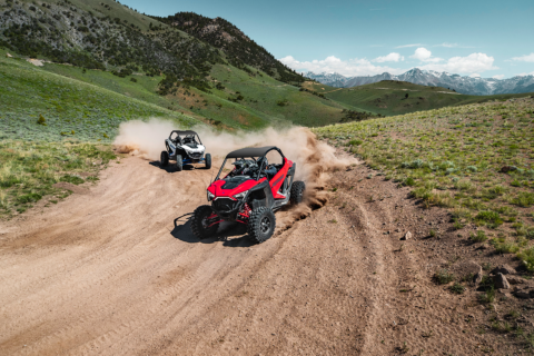 Two Polaris vehicles drive down a dirt road