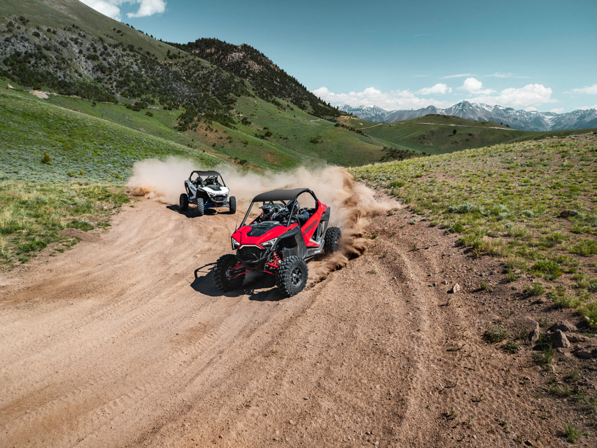 Two Polaris vehicles drive down a dirt road