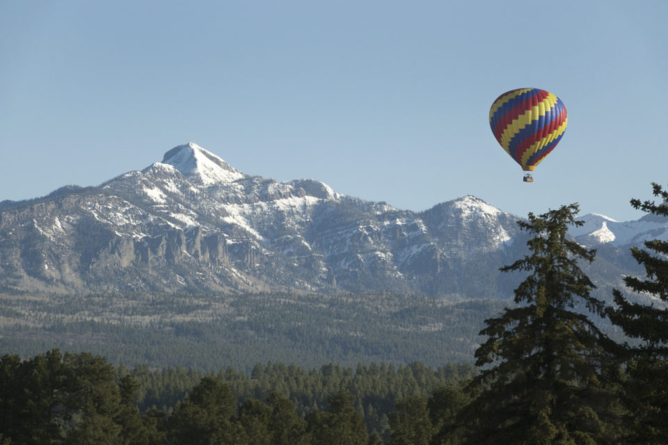 In the San Juan Range, a colorful hot air balloon floats over Pagosa Springs with the Pagosa Peak at an elevation of 12,640 feet in the background.