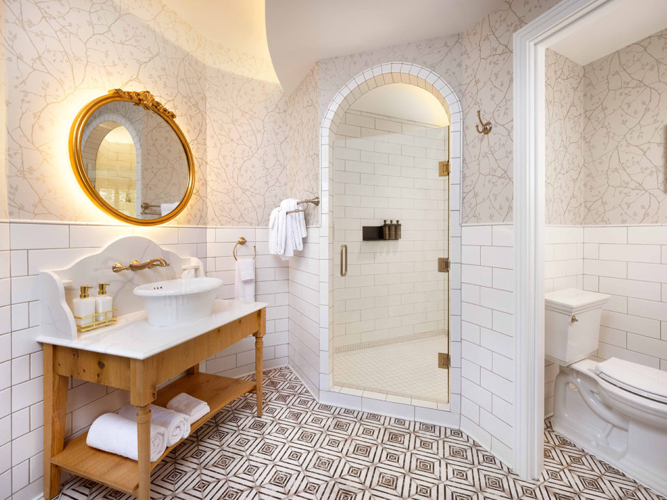 White bathroom with arched doorway shower, gold vanity