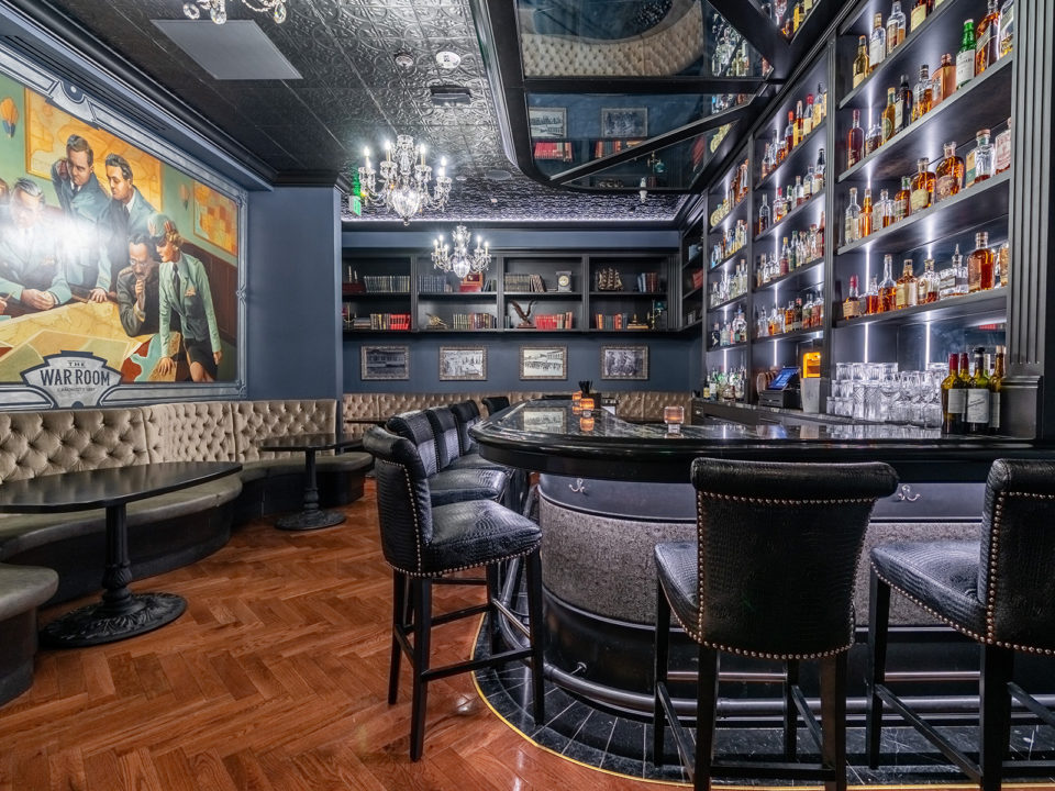 Cocktail lounge with dark blue walls, a bar with hightop chairs, and banquettes