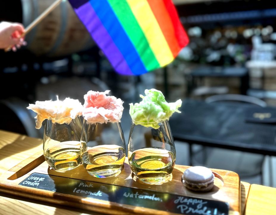 A wine flight with a rainbow Pride flag in the background