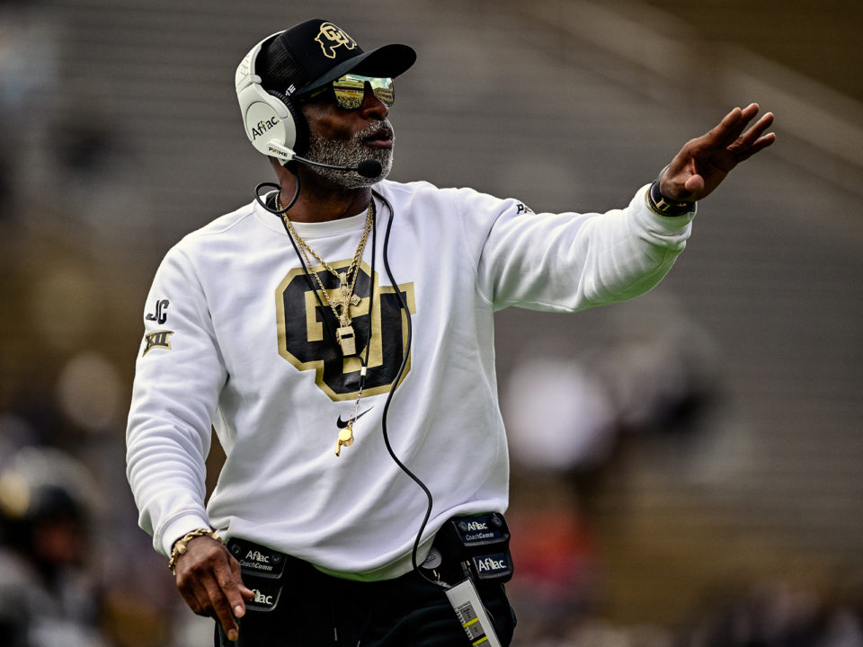 Deion Sanders wears a white CU sweatshirt and coaches on the sideline
