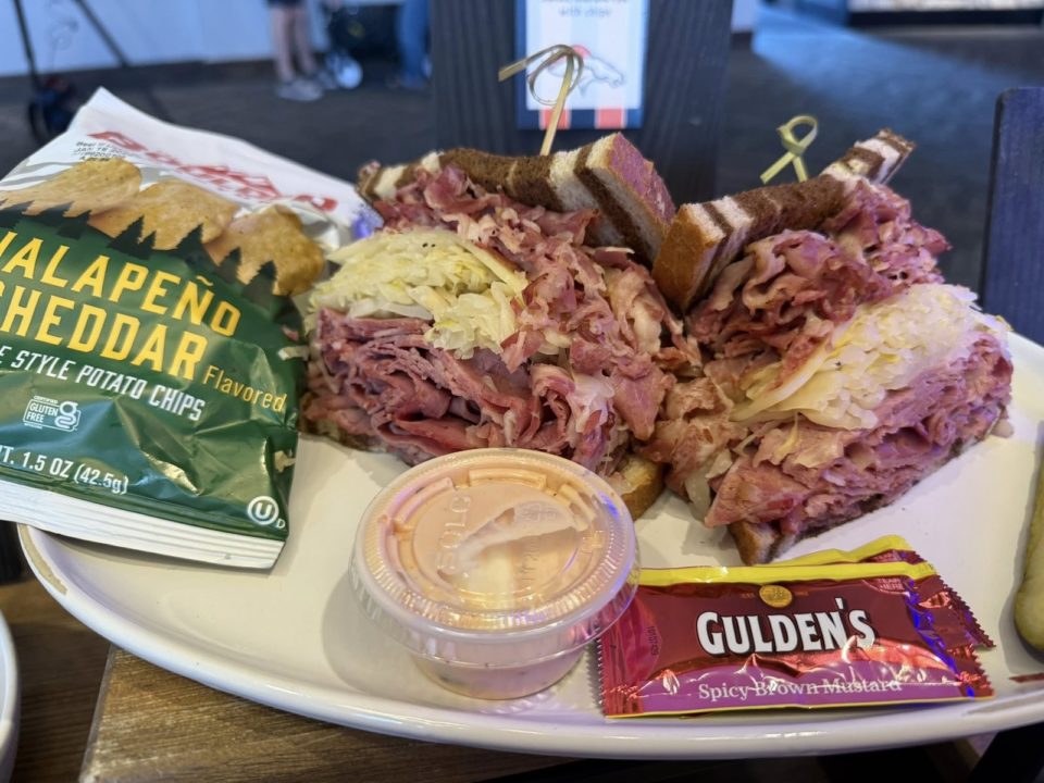 A reuben sandwich with a side of sauce, gulden mustard packet, and potato chip bag