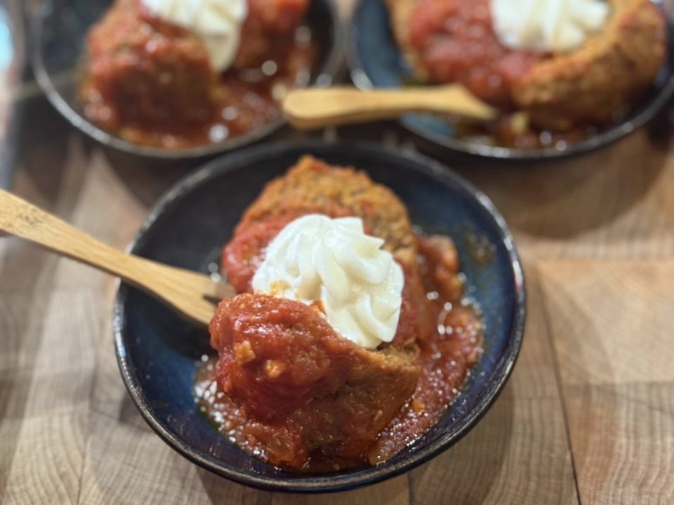 A meatball with sauce and ricotta cheese in a small black bowl