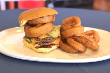 A double cheeseburger with onion rings on top and a side of onion rings