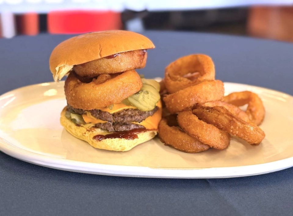 A double cheeseburger with onion rings on top and a side of onion rings