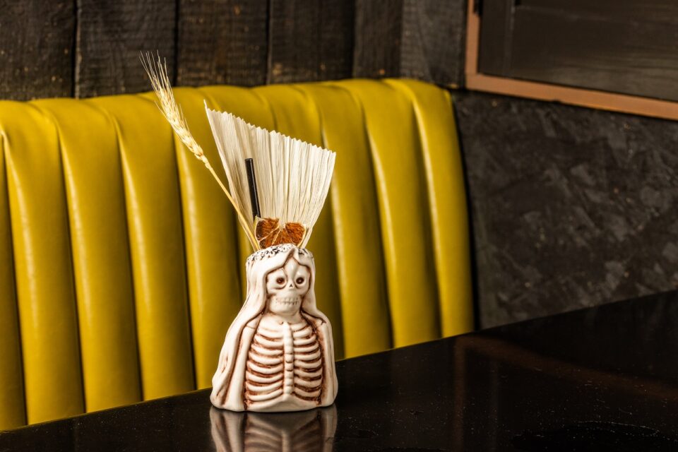 A cocktail mug shaped like a skeletal woman with garnishes and a straw