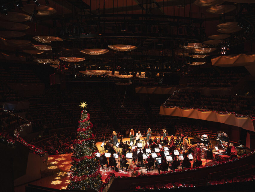An orchestra performing near a Christmas tree
