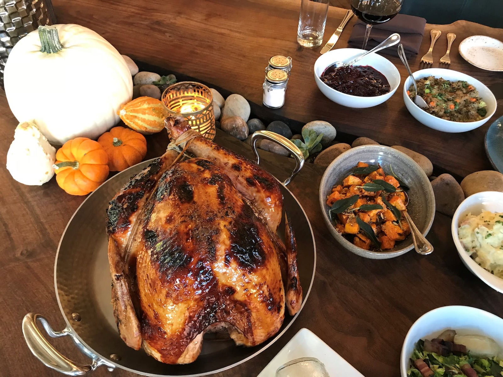 A whole roast turkey in a round pan surrounded by bowls of side dishes and several miniature pumpkins