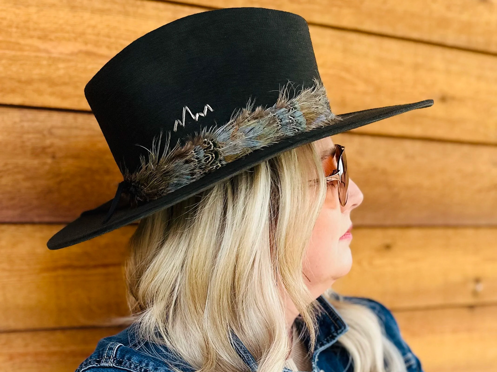 Woman wearing a black Western hat with feathers and a mountain embroidered on it