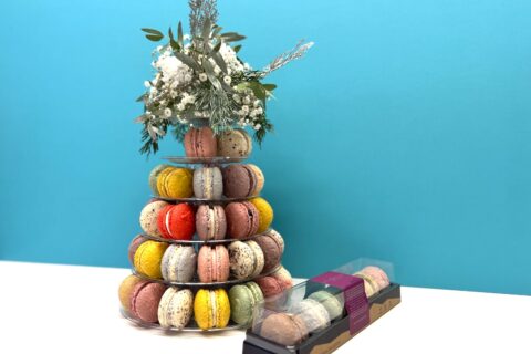 A tiered macron display topped with flowers next to a small box of macarons.