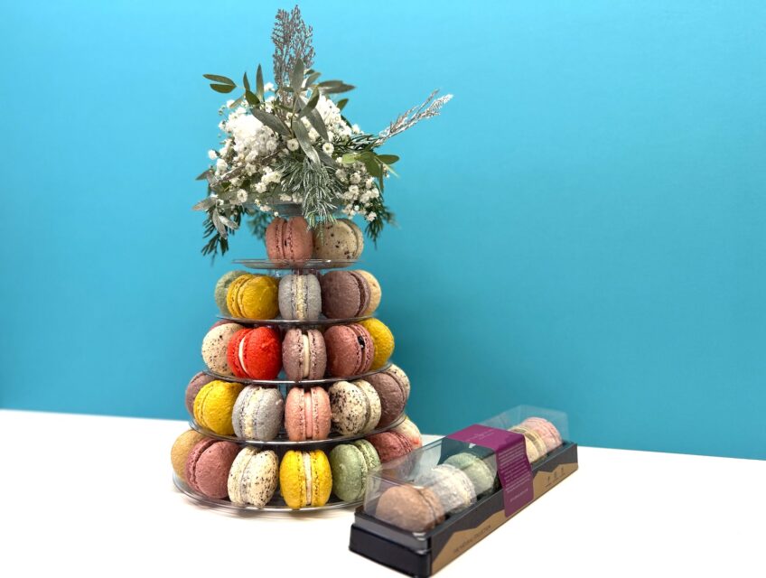 A tiered macron display topped with flowers next to a small box of macarons.