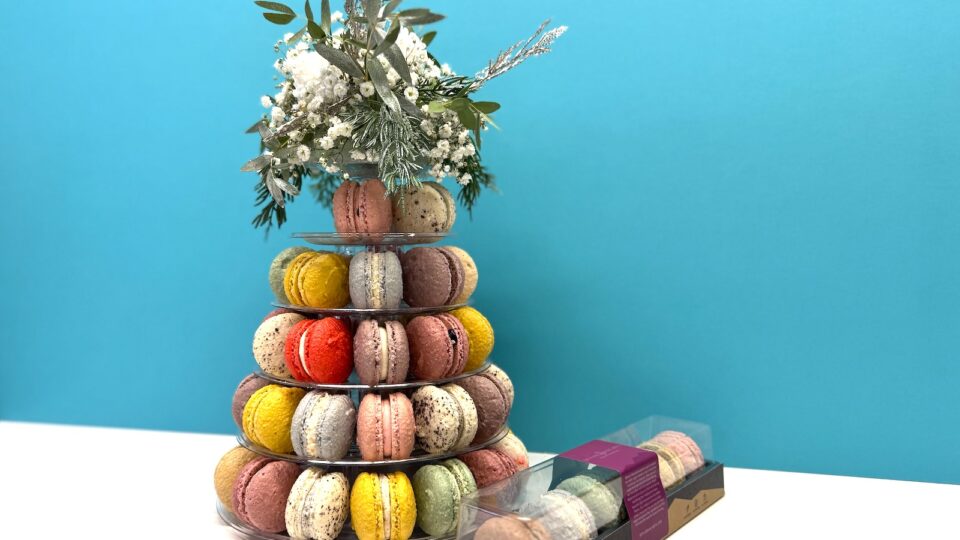 A tiered macron display topped with flowers next to a small box of macarons.