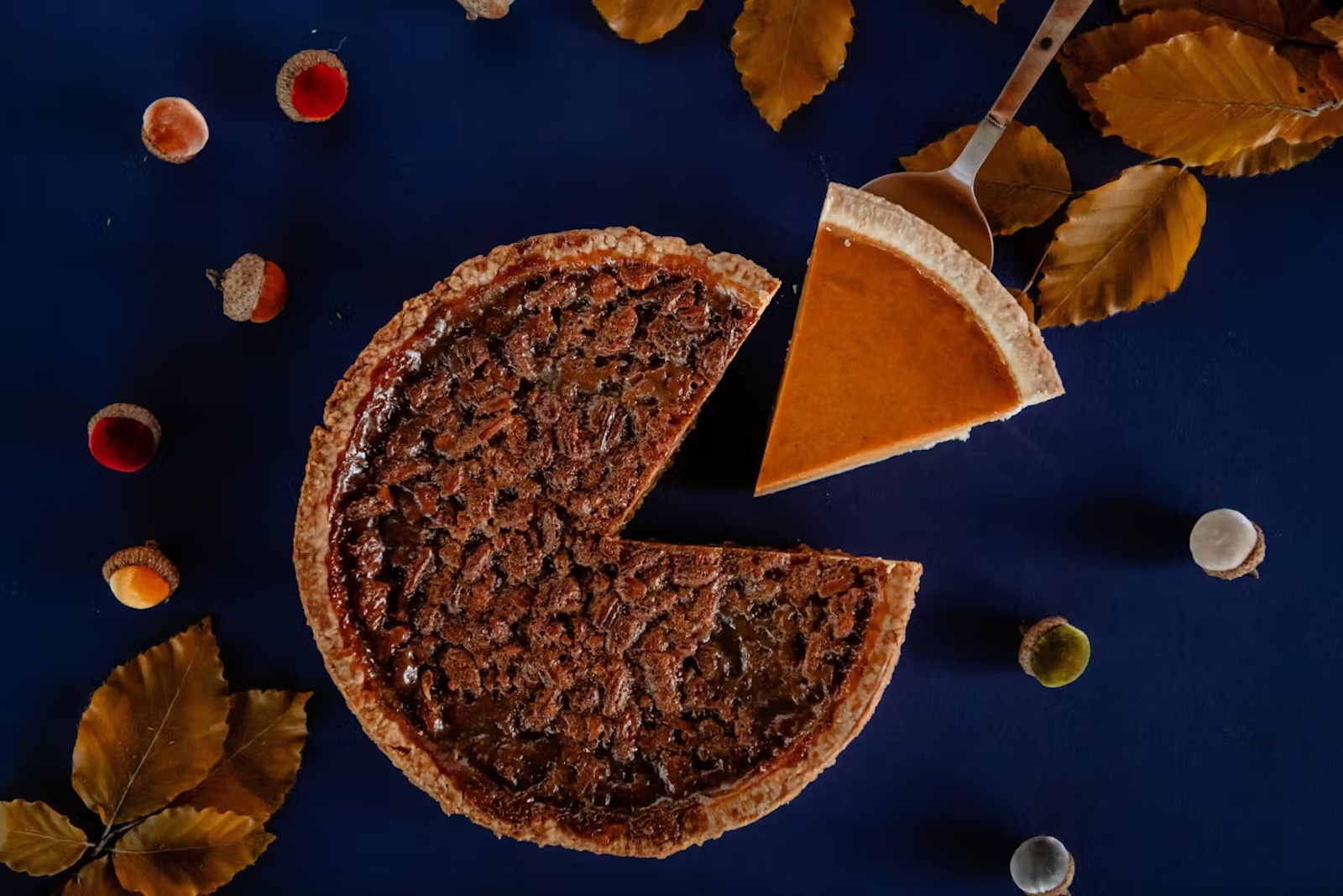 A pecan pie with one sliced removed and a slice of pumpkin pie on a spatula
