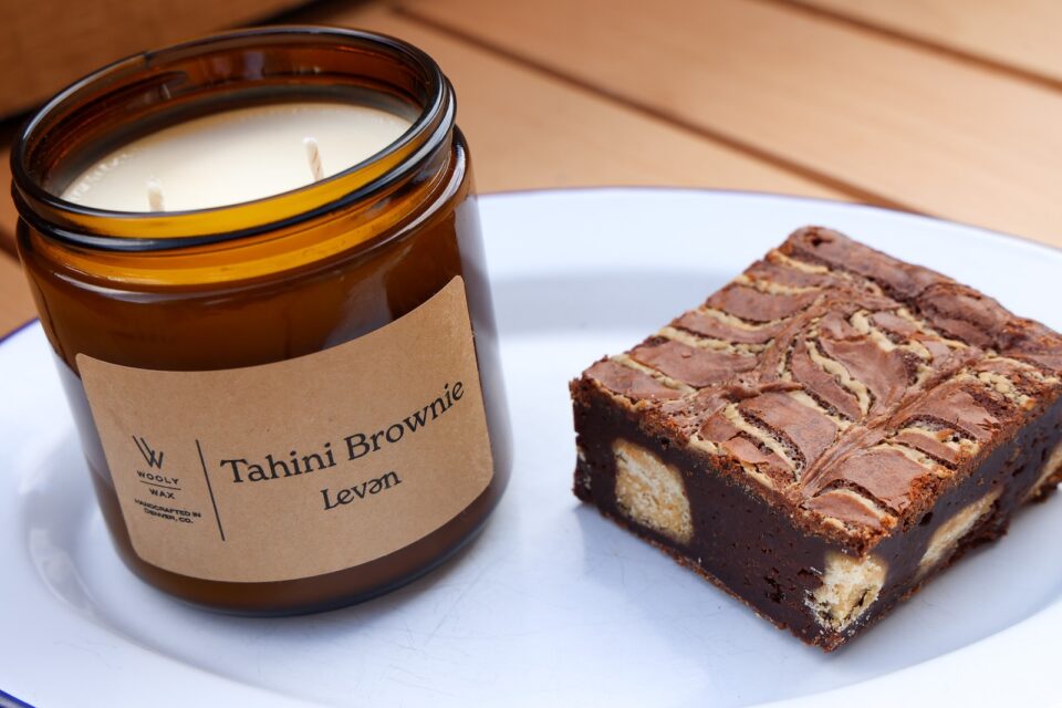 A candle in a brown glass jar next to a brownie.