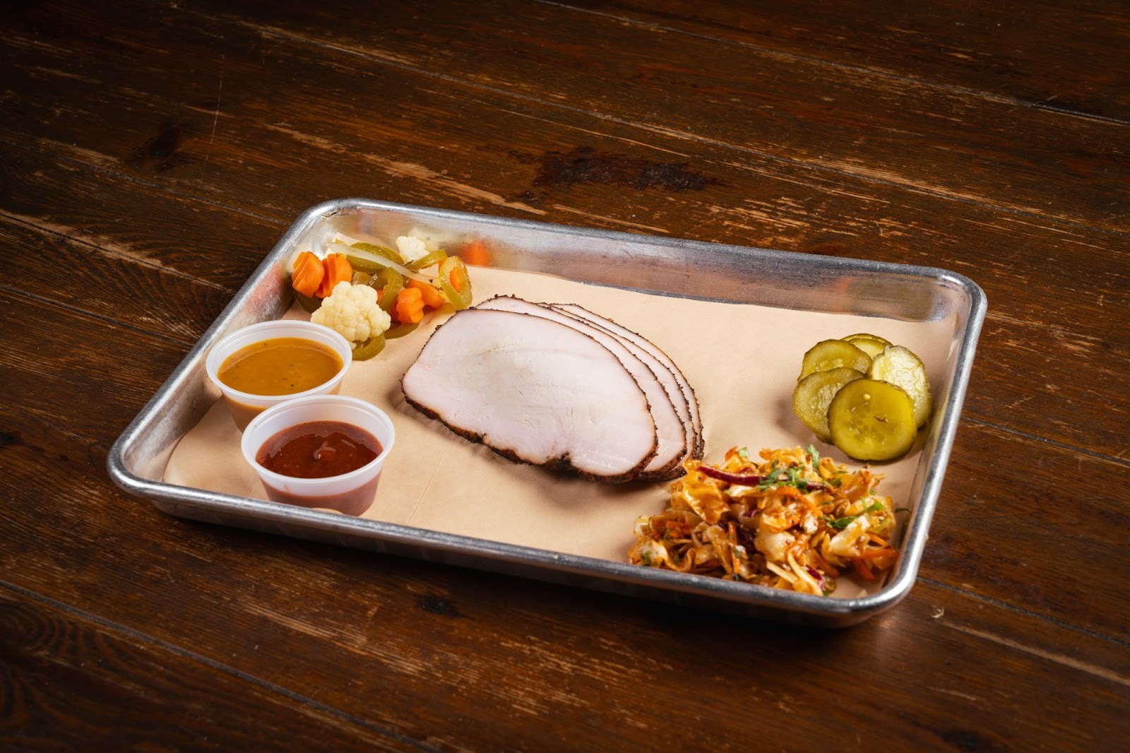 A paper lined tray of smoked turkey slices with sauces in cups and vegetable sides