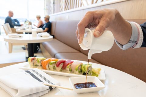 Pouring a white sauce or dressing onto a plate of sushi rolls at a restaurant.