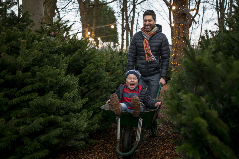 A father giving his son a wheelbarrow ride at a Christmas market in Northeastern England. They are wearing warm clothing and having fun.