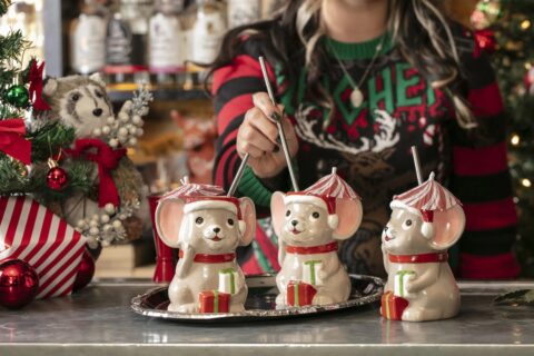 Three Christmas mouse-shaped cocktial mugs with straws and a woman in a Christmas sweater (face not shown)