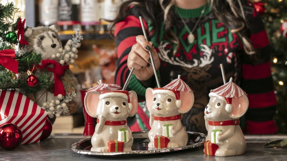 Three Christmas mouse-shaped cocktial mugs with straws and a woman in a Christmas sweater (face not shown)