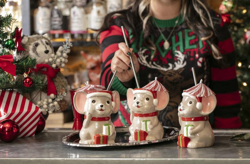 Three Christmas mouse-shaped cocktial mugs with straws and a woman in a Christmas sweater (face not shown)