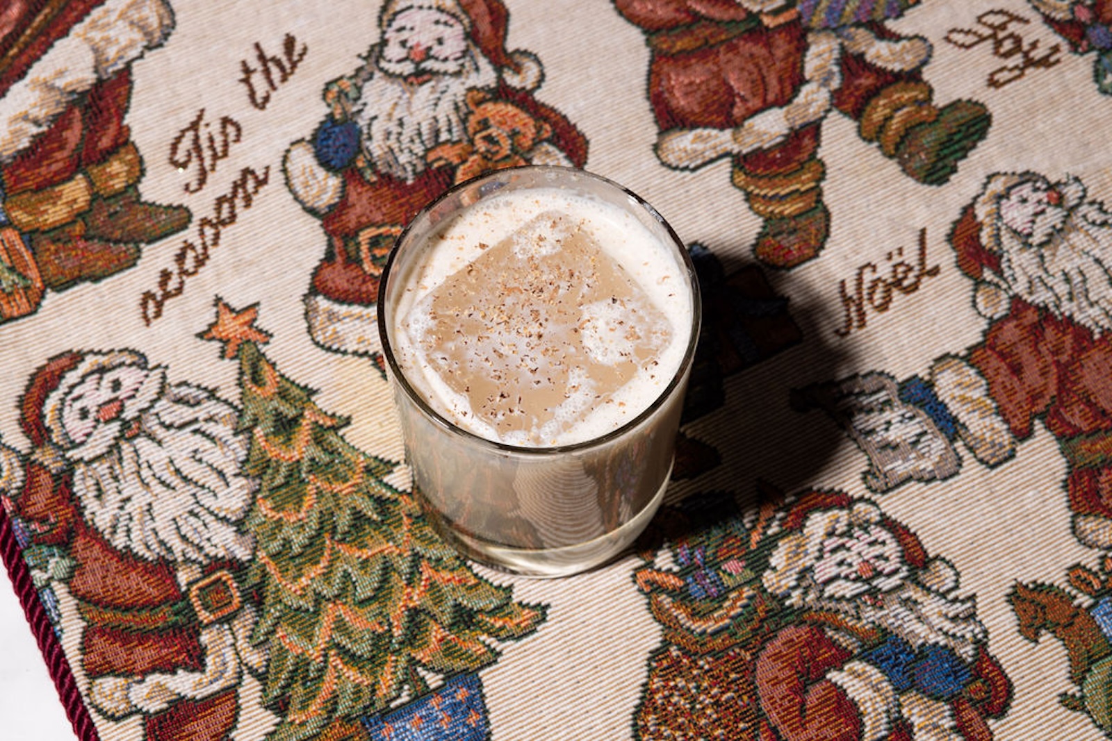 A creamy cocktail on ice in a rocks glass with Santa Claus fabric underneath