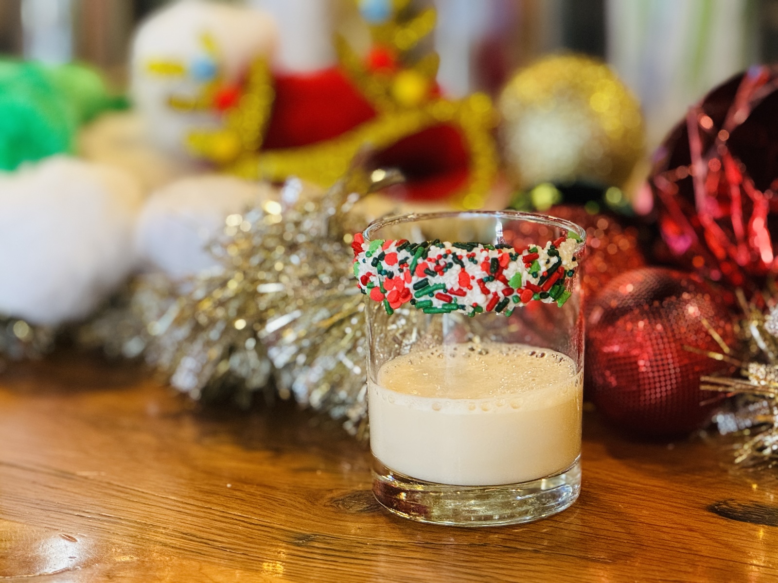 A milky cocktail in a short glass with red, white, and green candy sprinkles on the rim