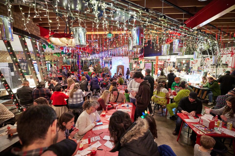 A large group of people at multiple tables play bingo with Santa Claus in a Christmas decorated ice cream shop
