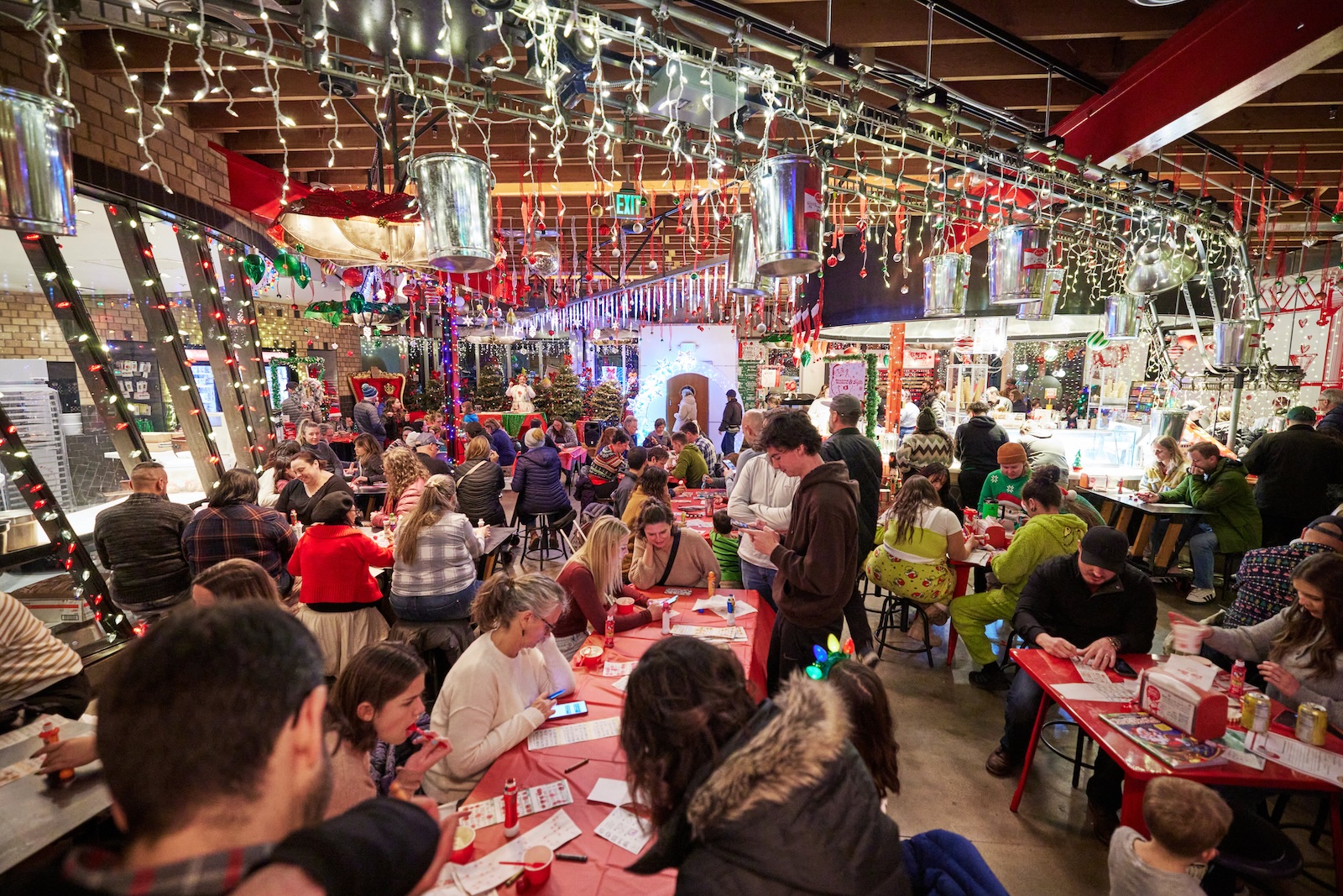 A large group of people at multiple tables play bingo with Santa Claus in a Christmas decorated ice cream shop