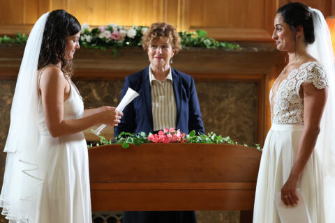 Two women in wedding dresses stand at an altar