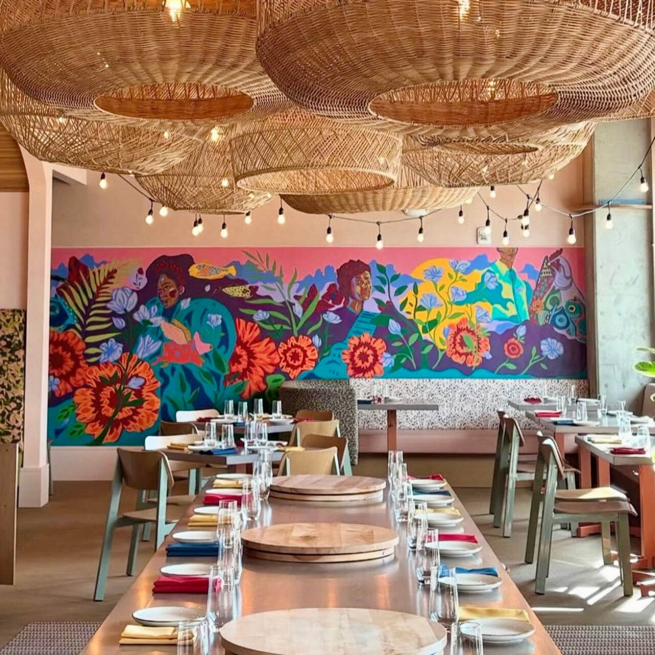 Long communal table with woven pendant lights hanging over it and a mural behind it.