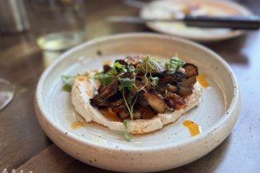 A white ceramic bowl holds sauteed mushrooms on top of whipped tahini