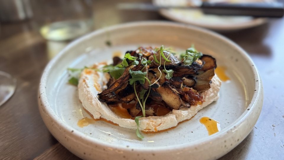 A white ceramic bowl holds sauteed mushrooms on top of whipped tahini