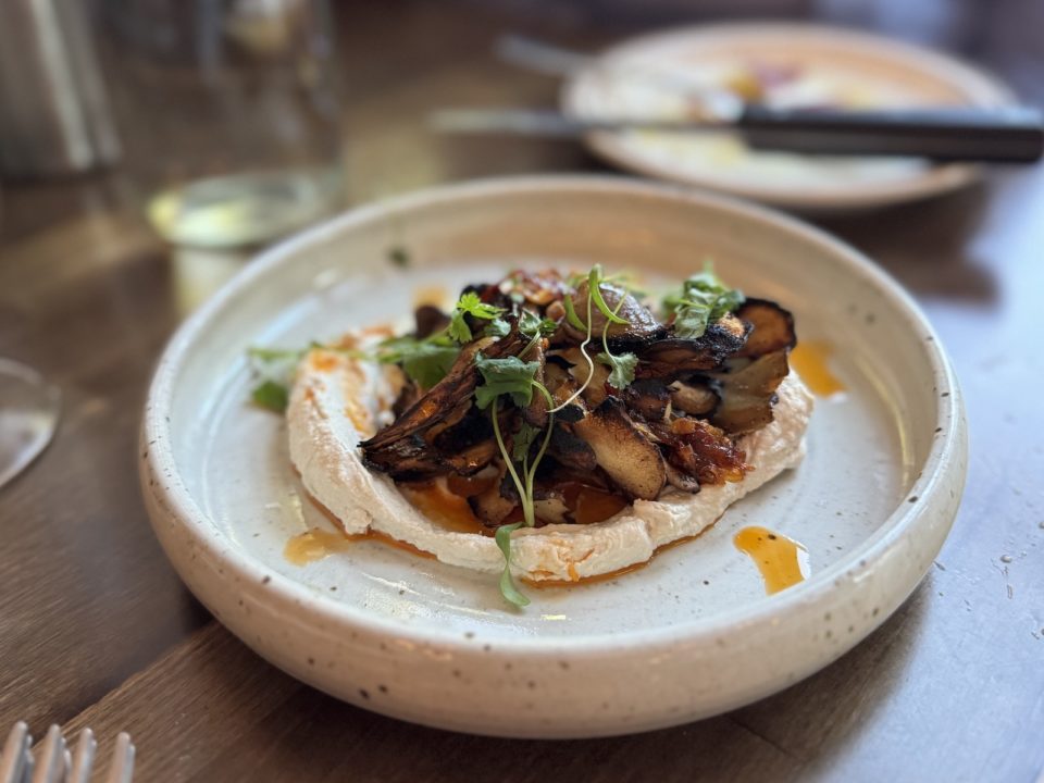A white ceramic bowl holds sauteed mushrooms on top of whipped tahini