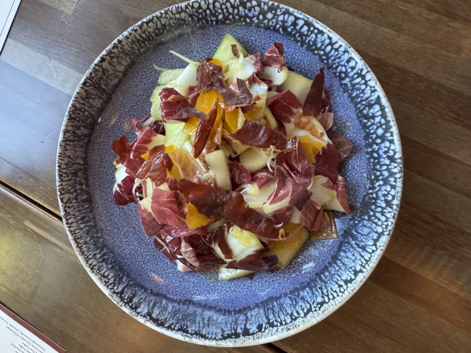 A blue ceramic bowl of salad with red cabbage, honeydew, and other vegetables