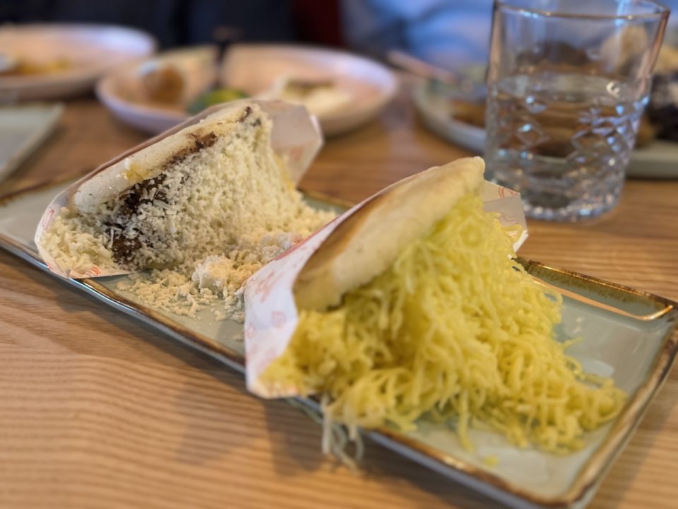 Two Venezuelan areps overflowing with shredded cheese on a rectangular plate.