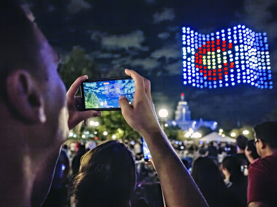 Someone takes a picture on their phone of a drone show in Denver
