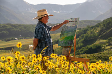 A man paints outdoors in a field of wildflowers
