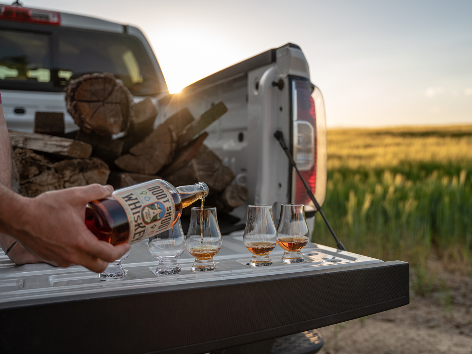 Man pours whiskey into glasses sitting on a tailgate